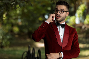 handsome businessman wearing red tuxedo talking on the phone astonished