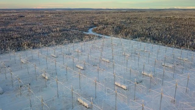 Aerial, drone shot, panning over the HAARP antenna array, in middle of Alaskan forest, at golden hour, on a sunny, winter evening, in Gakona, Alaska, USA