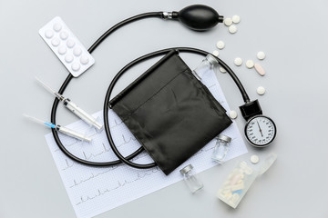 Sphygmomanometer, cardiogram and pills on light background