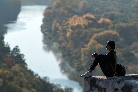 Beautiful girl sits on a hill and looks into the distance. Enjoyment of nature