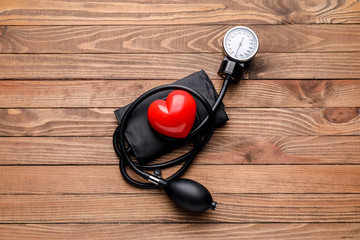Sphygmomanometer and red heart on wooden background