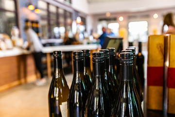 wine bottles, dark amber glass with black screw cap seal closeup selective focus, people buying and tasting wines in the background
