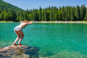 Attractive brunette jumping into crystal clean forest lake enjoying the summer.