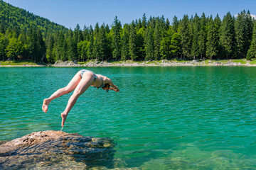 Attractive brunette jumping into crystal clean forest lake enjoying the summer.