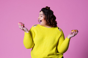 Cheerful plus size model with doughnuts, happy fat woman on pink background