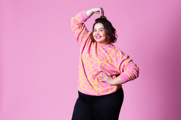Happy plus size model in casual clothes, fat woman on pink background