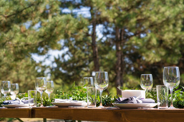 Beautifully decorated wooden table in a summer open-air cafe. Green branch and fresh flowers table decoration