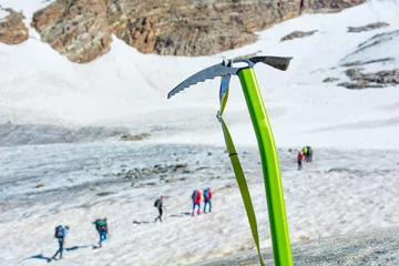 Fotobehang Ice axe positioned in snow with mountaineers walking in the background. © anzebizjan