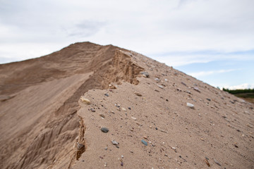 Large pile of yellow sand, against the sky, on a summer day. Quarrying and mining of building material.