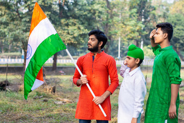 Three kids and young boys of different age and different religion hearing tricolor dress and holding Indian National flag. Indian kids celebrating Republic or Independence day of India. 
