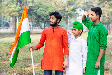Three kids and young boys of different age and different religion hearing tricolor dress and holding Indian National flag. Indian kids celebrating Republic or Independence day of India. 
