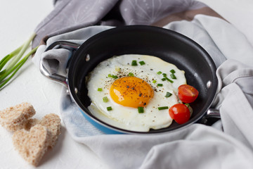 Fried egg with tomato and chopped green onion in frying pan, sliced bread in shape of heart. Tasty romantic breakfast