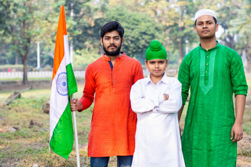 Three kids and young boys of different age and different religion hearing tricolor dress and holding Indian National flag. Indian kids celebrating Republic or Independence day of India. 