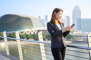Fototapeta premium Young Asian business woman with Phone standing outdoors using smartphone in modern city financial district. Business and Communication concept
