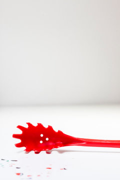 cucharon rojo de pasta sobre mesa blanca con restos de pintura