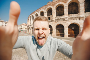 Happy male traveler makes selfie photo on background of amphitheater coliseum in city Verona Italy....