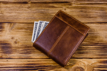 Brown leather wallet and one hundred dollar banknotes on the wooden background