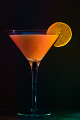  Martini glass with orange cocktail and slice of fruit - black background