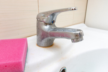 Sponge for washing dirty faucet with limescale, calcified water tap with lime scale on washbowl in...