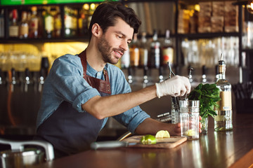 Drink Preparation. Bartender standing at counter mixing ingredients in glass concentrated