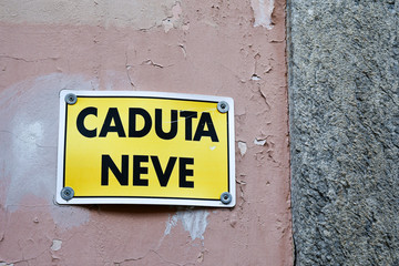 Close-up of an old wall with a warning sign that says: "Snow fall" (Italian: Caduta neve), warning of the danger of falling snow from the roofs of houses, Dronero, Cuneo, Piedmont, Italy