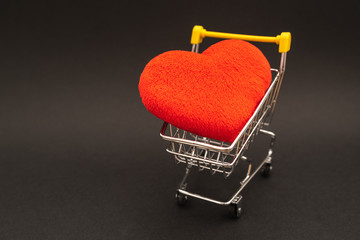 Red heart in shopping trolley on black background