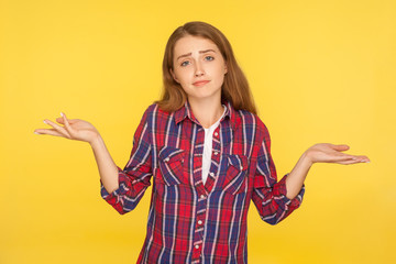 I don't know! Portrait of confused puzzled ginger girl in checkered shirt raising hands in questioning gesture, no idea, having clueless uncertain face, doubting. indoor studio shot, yellow background