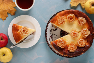 Cheesecake with apples and cup of coffee located on a light blue background, decorated with roses from apples, Top view