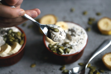 Male hands hold a bowl of yogurt. A man with a spoon eats yogurt with seeds. Chia pudding with pumpkin seeds and banana. Healthy breakfast or snack. Keto diet. Keto dessert. Sugar free dessert
