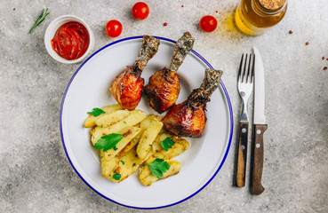 Grilled chicken drumstick bbq with potato slices on enameled plate stone gray background.