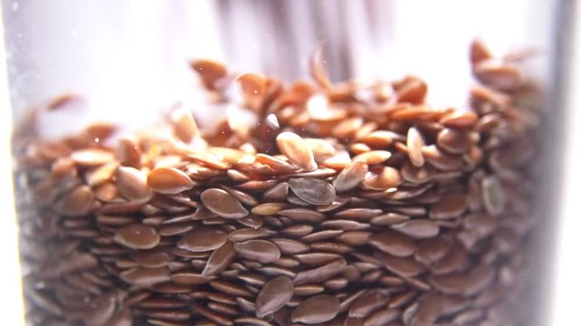 Flax seeds pouring into glass macro