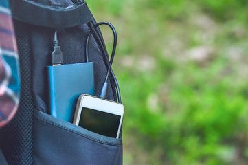 A power bank charges a smartphone in a pocket of a black backpack, on a background of grass.