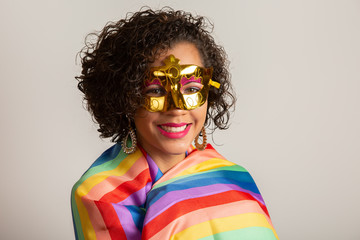 Young curly hair woman in costume enjoying the carnival party covering with lgbt pride flag. Alone. One. Keeping fist up, covering LGBT flag. LGBT+ flag on white background.