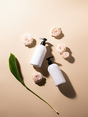White bottles of gel and shampoo on a beige background with roses