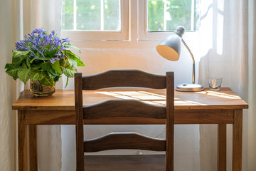 Wooden table with chair, lamp and a bouquet of flowers near the window in modern working area at home