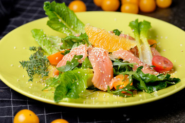 Cold salmon salad with green leaves, cucumber, avocado, lime and tomato on black stone background. Top view with copy space. Rustic style.