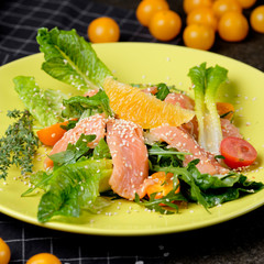 Cold salmon salad with green leaves, cucumber, avocado, lime and tomato on black stone background. Top view with copy space. Rustic style.