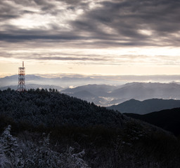Communication tower on snow covered mountain overlooking misty valley at sunrise