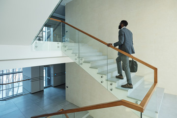 Young elegant African businessman with black leather handbag going upstairs