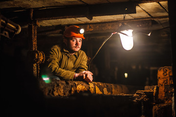 A tired miner in a coal mine looks at the light. Work in a coal mine. Portrait of a miner. Copy...