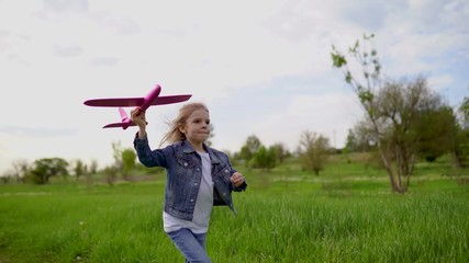 Little girl launches a toy plane into the air in the park outdoor. Child launches a toy plane. Beautiful little girl running on the grass and launches a pink toy plane. Slow motion