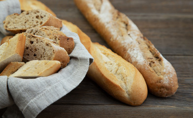 Whole-grain and traditional baguettes lie next to a wicker basket with a linen napkin and slices of bread. Wood background. Bakery. Bread