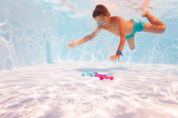 Little boy swim underwater in the pool wearing googles side view diving to get the toy