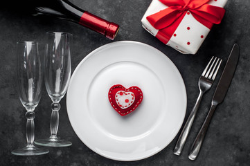 Table setting for Valentine's Day - white plate, wine, gift, kitchen appliances, hearts on a stone background