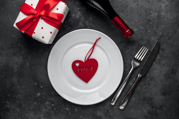 Table setting for Valentine's Day - white plate, wine, gift, kitchen appliances, hearts on a stone background