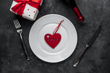 Table setting for Valentine's Day - white plate, wine, gift, kitchen appliances, hearts on a stone background