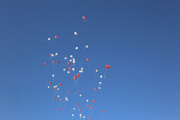 White and red heart balloons in the blue cloudless sky