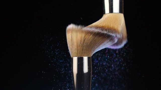 Different makeup brushes with powder flying on black background