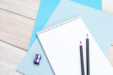 Notepad for notes, a pair of pencils, a purple pencil sharpener and sheets of blue cardboard on a white wooden table.