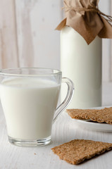 A glass bottle with kefir with bread rolls on the wooden table